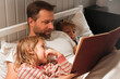 © Marina Demidiuk - Happy mature 40 year old father reading book to his curious children lying in a bed before the sleep. Dad, little daughter and son spending time together. Family read the fairy story. Evening bedroom.