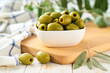 © Igor Dudchak - pitted olives in a bowl with fresh olive leaves. Greens pitted olives on a white wooden table.