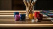 © MUCHAMAD - Paints in jars with paintbrushes in glass, natural light on a wooden table