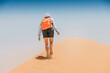 © EdNurg - Female tourist trekking up a sandy dune in the desert under a bright sun, embracing the adventure and beauty of the vast landscape