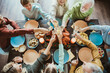 © deagreez - Family Thanksgiving gathering around a long table to celebrate with friends and relatives toasting with glasses and sharing turkey and feast during a warm holiday dinner