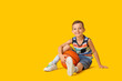 © Pixel-Shot - Stylish little boy with ball sitting on yellow background