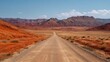 © backup_studio - Long gravel road winding through a vast desert landscape with rugged red rock mountains under a clear blue sky. Travel and adventure concept.