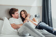 © Daniel - A young couple lies in bed, laughing and playfully teasing each other. Their smiles and playful touches show joy, closeness, and love, sharing a fun, relaxed moment at home.