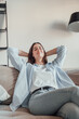 © Daniel - Relaxed serene pretty young woman feel fatigue lounge on comfortable sofa hands behind head rest at home, happy calm lady dream enjoy wellbeing breathing fresh air in cozy home modern living room