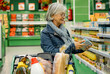 © luciano - Smiling senior woman with glasses pushing a shopping cart at the supermarket shopping with attention to quality and prices - Concept of consumerism, price rise, inflation
