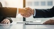 © Farhan - Close-up of a business handshake over a desk with a clipboard and paperwork, representing the finalization of a contract in a formal meeting.