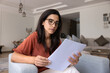 © fizkes - Serious young Latin woman reading paper financial document