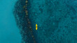 © Photo Sesaon - aerial view  woman bright yellow kayak with  in the vast expanse of crystal clear turquoise water. The seabeds rocky texture is visible beneath the surface, concept marine environment.