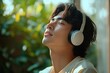 © zhuan - Young man wearing white headphones with eyes closed enjoying music with a peaceful and relaxed expression outdoors surrounded by greenery