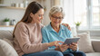 © Olga - Young woman and elderly lady using tablet together on sofa