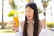 © luismolinero - Pretty Chinese woman holding an orange juice at outdoors celebrating a victory