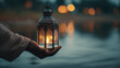 © tiagozr - Hand holding glowing lantern by water during Ramadan evening