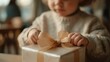 © CYBERPINK - Close-up of a young child's hands holding a small gift box. the child is wearing a beige sweater and appears to be around 2-3 years old.