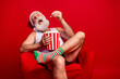 © deagreez - A cheerful grandpa Santa sits in a red chair eating popcorn from a striped bucket