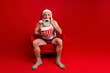 © deagreez - Santa in red chair with popcorn on bright Christmas backdrop in funny festive pajama scene