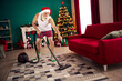 © deagreez - Santa Claus doing household chores in festive attire near a decorated Christmas tree inside a cozy home