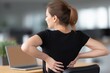 © Klay - Woman experiencing lower back pain while sitting at desk in modern office workplace health issue