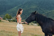 © SHOTPRIME STUDIO - A young woman in casual attire stands in a sunlit field, tenderly offering her hand to a calm horse, creating a peaceful, intimate moment in nature.