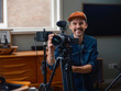 © Victor - Videographer presenting camera equipment to viewer with confident expression in residential studio