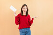 © sitthiphong - Happy Asian business woman standing and hold blank paper or gift voucher mockup on beige color background.