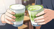 © Siuzenn - Two people raise their refreshing matcha green tea lattes in a delightful toast, celebrating a shared moment of tranquility and taste in a cozy cafe setting