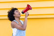 © VISTA by Westend61 - Woman shouting with red megaphone in front of a yellow wall