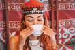© EdNurg - Young woman wearing a traditional Kyrgyz kalpak, savoring a cup of tea inside a cozy yurt, embracing the rich culture of Kyrgyzstan