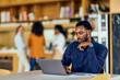 © bnenin - African-American Man Working On Laptop in Modern Coffee Shop Library Setting, Focused and Thoughtful