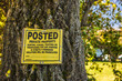 © StockMediaSeller - Yellow posted private property sign nailed to a tree trunk, warning against trespassing, hunting, and fishing on private land