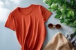 © Iryna - Red t-shirt and accessories flat lay with sunglasses, knit blanket, and greenery on light surface