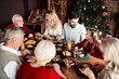 © deagreez - Family gathers for a festive Christmas meal around a large table in a cozy home setting with a decorated tree and warm lights