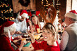 © deagreez - Family gathers for Christmas dinner at a warm home filled with lights and decorations as a young woman wears reindeer antlers and friends and relatives share joy and celebrate together