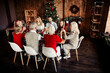 © deagreez - Family Christmas feast around a wooden table in a cozy living room with a decorated tree and warm lights creating a festive holiday atmosphere