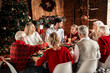 © deagreez - Family gathers for a warm Christmas dinner at home around a festive table with tree lights and holiday decorations