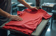 © Vadym - Man operates heat press machine to apply design on red t-shirt. Person customizes apparel in workshop. Production of branded merchandise for sale.