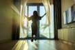 © shine - Excited happy woman opens the curtains white waving curtain, relaxes in sunlight, enjoying a peaceful moment in living room. The room is bathed in natural light, evoking calm and warmth. Good morning.