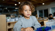 © Milos - A child is concentrating on arranging colorful blocks, demonstrating problem-solving skills and creativity in a playful learning environment with peers in the background.