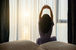 © shine - Stretching after the sun. Middle aged woman with long hair is waking up in the morning, stretches in the bed, do simple exercise, Sunshines on her from the big window. Exuding confidence and style.