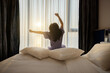 © shine - Good morning, New day, Holiday. Happy asian middle aged woman wake up on bed, stretching her arms in fresh early morning, relax peaceful morning routine. Luxury hotel or home in the morning sunlight.
