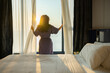 © shine - Healthy sleep, Recreation and Relaxation Concept. Happy middle aged woman waking up in bedroom and opens the curtains to let the Soft morning sunlight streaming through window. Greeting new day.