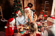 © deagreez - Family Christmas dinner around a festive table at home with a decorated tree twinkling lights warm atmosphere and joyful smiles