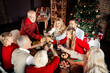 © deagreez - Family and friends celebrate Christmas together around a festively lit table with a Christmas tree and warm decorations