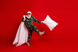 © deagreez - Cheerful santa in green pajama kicks a pillow on a bold red studio background creating a playful festive christmas mood