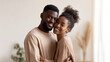 © dinatychynska - Happy African American couple embracing and smiling at camera in bright home interior. Young man and woman showing love, affection and joyful relationship. Valentine's day romance and togetherness.