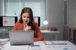© Tj - Asian businesswoman working on laptop, intently focusing on financial data and statistics, managing business paperwork in a contemporary office setting