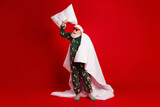 Santa in festive pajama poses with pillow under a red background wrapped in a white blanket for a humorous Christmas stock photo