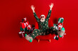 © deagreez - Cheerful Santa in festive pajama suit sits in red chair surrounded by gifts with striped socks celebrating christmas eve at home