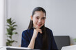 © amnaj - Young Asian businesswoman smiling, holding a pen, working with an open notebook at an office desk. Focus on professionalism and success