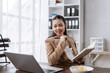 © amnaj - Asian businesswoman working at desk, smiling while holding a pen and notebook, planning tasks in a modern office setup